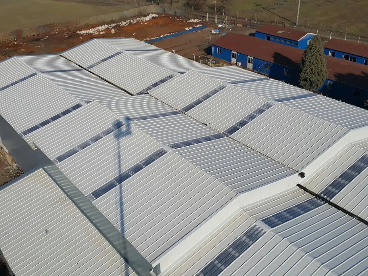 Geniş endüstriyel yapılarda tamamlanmış beyaz panel çatı uygulamalarının üstten görünümü